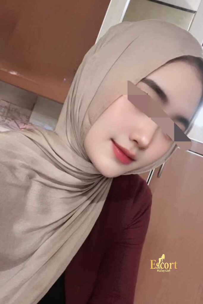 Escort Malay Girl Amina, a 22-year-old petite Malay escort, smiling in a hijab and maroon top. KL Escort Girl Service