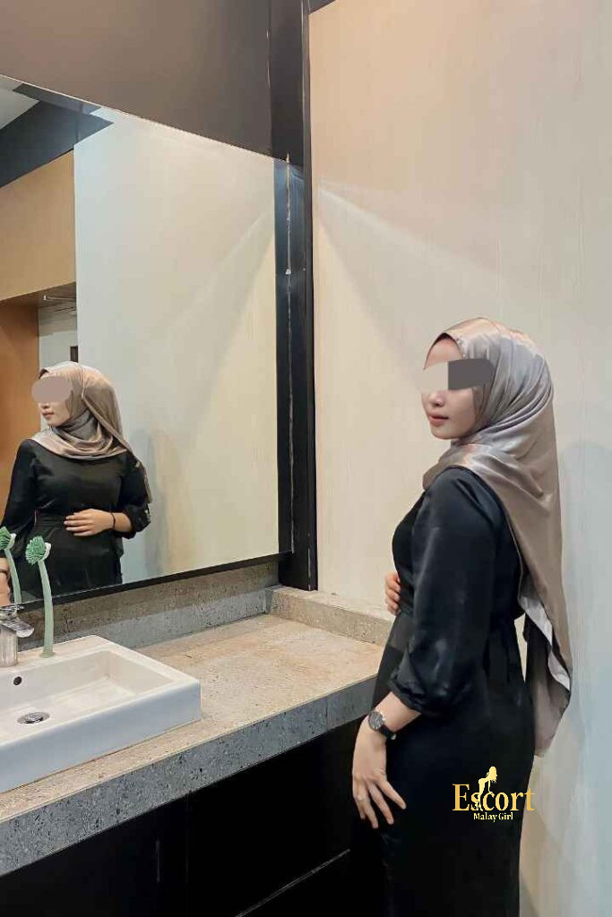Escort Malay Girl Eika Malay Escort standing near a bathroom sink, wearing a black dress and hijab KL Escort Girl Service