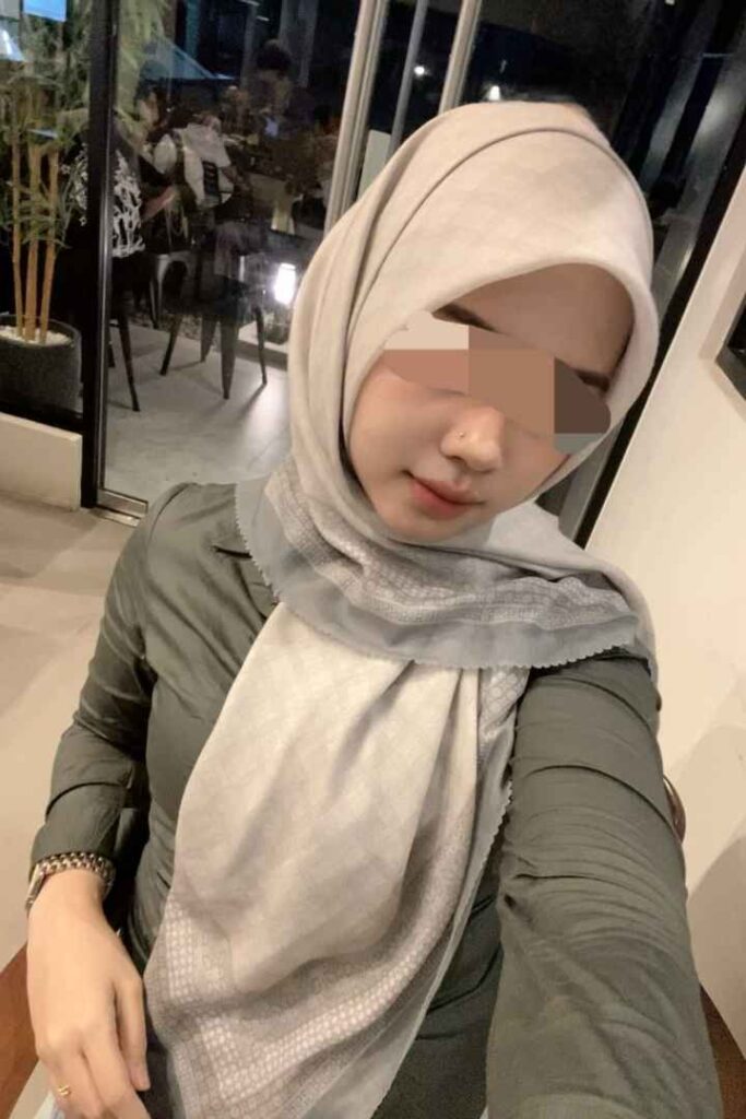 Escort Malay Girl Woman in hijab and green top sitting with blurred background KL Escort Girl Service