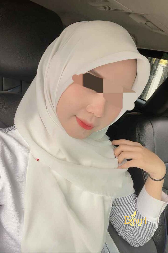 Escort Malay Girl Woman wearing a white hijab sitting in a car, smiling and posing for a picture KL Escort Girl Service