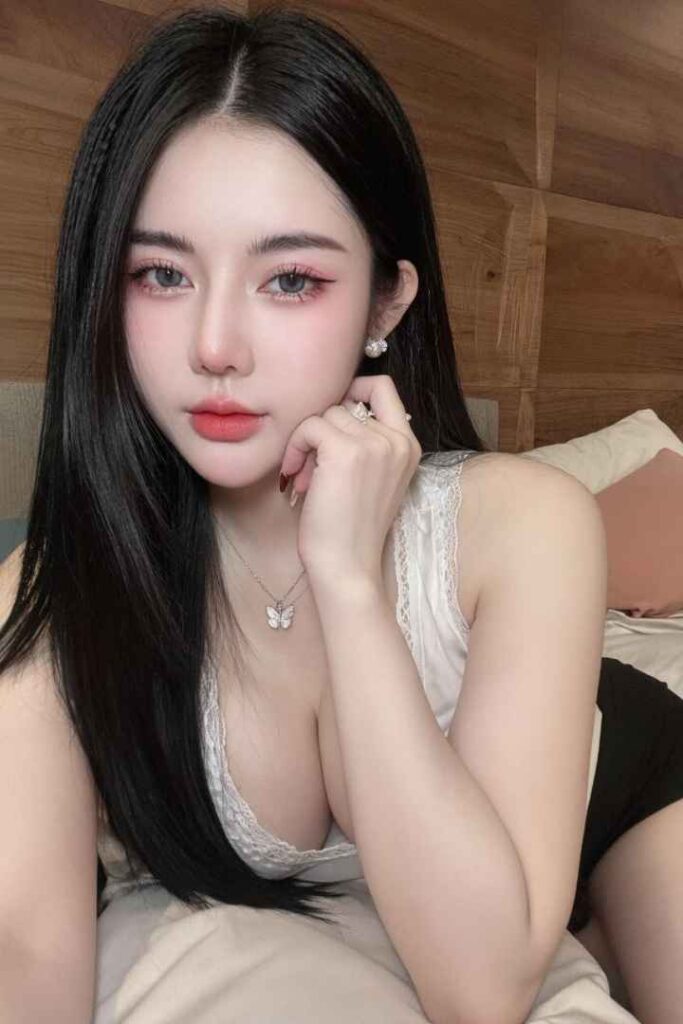 Escort Malay Girl Young woman with long dark hair and makeup, wearing a white lace top and a butterfly necklace. KL Escort Girl Service