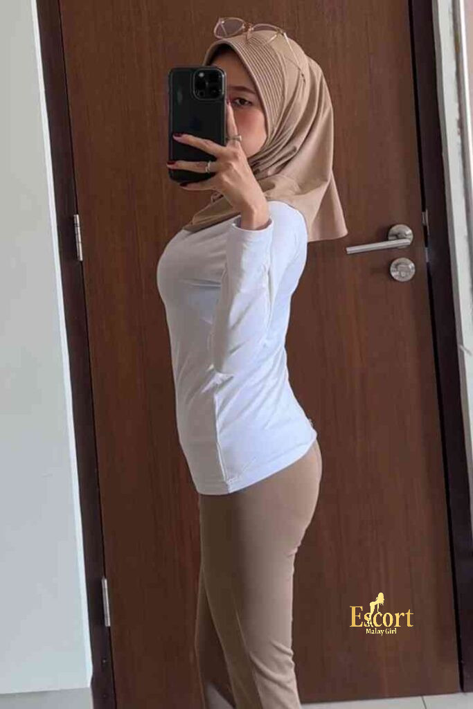 Escort Malay Girl Kirana, a 23-year-old Malay escort in KL, taking a selfie in a white top and beige pants. KL Escort Girl Service