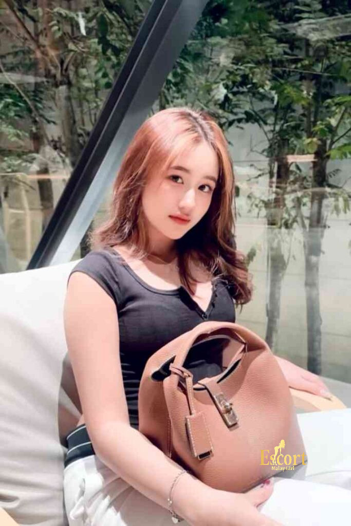 Escort Malay Girl Laila Malay Escort in black shirt holding a brown handbag, sitting on a white couch KL Escort Girl Service