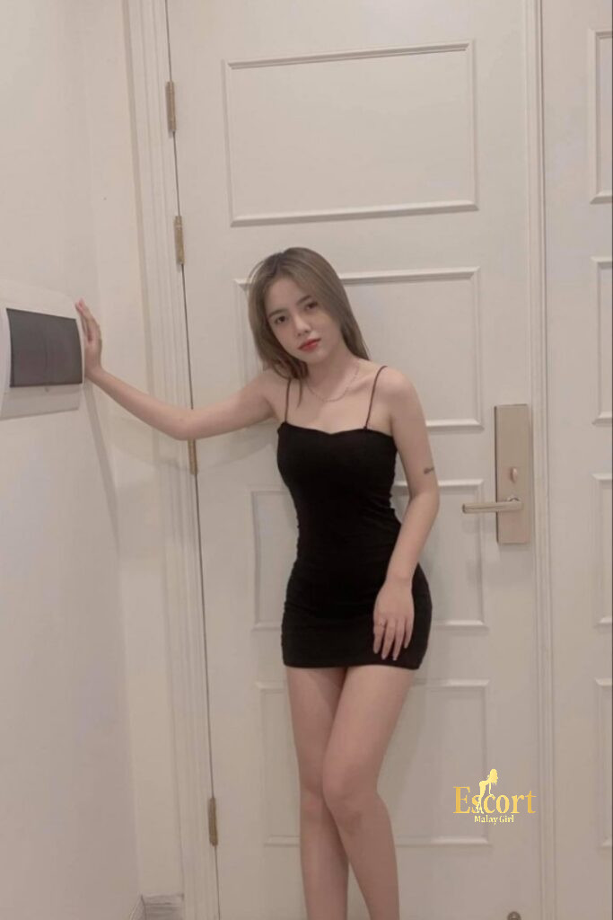 Escort Malay Girl Sally Vietnam Escort, wearing a black dress, standing in front of a white door KL Escort Girl Service