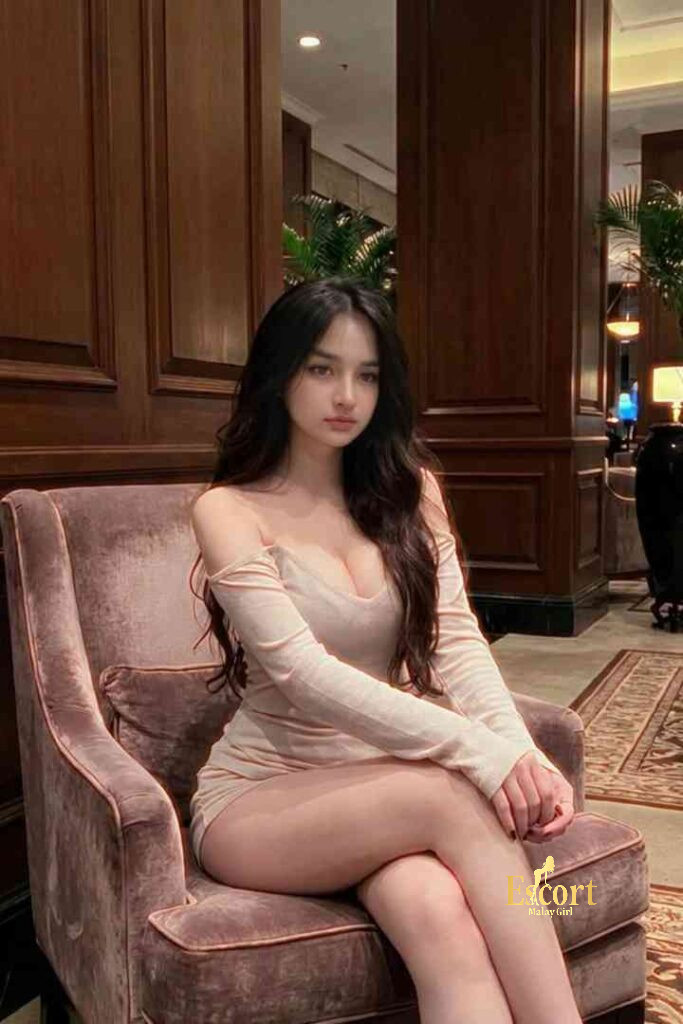 Escort Malay Girl Ummi, a 22yo Malay escort in a pink dress, sitting on a chair in a hotel lobby KL Escort Girl Service