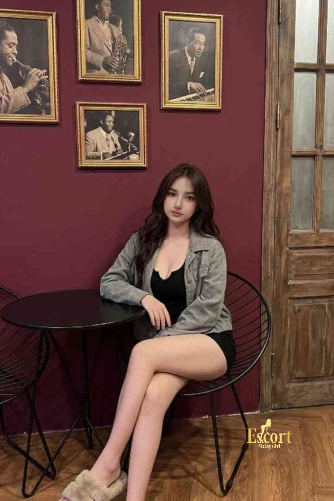 Escort Malay Girl Ummi, a 22yo C Cup Malay Escort, sitting in a room with framed musical portraits KL Escort Girl Service