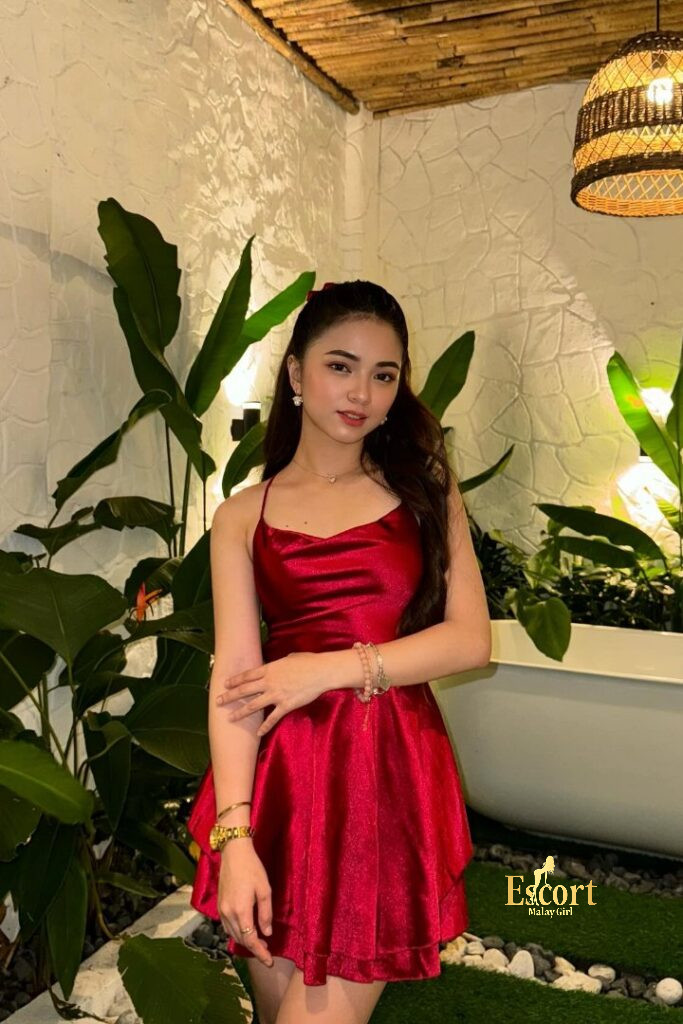 Escort Malay Girl Zanis, 22yo Malay Escort in a red dress, posing near green plants and a bathtub KL Escort Girl Service