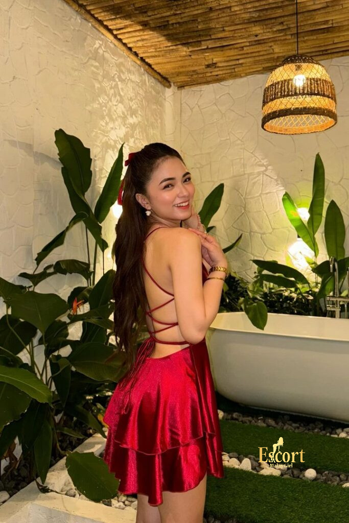 Escort Malay Girl Zanis, 22yo Malay escort, wearing red dress, smiling next to plants and bathtub KL Escort Girl Service