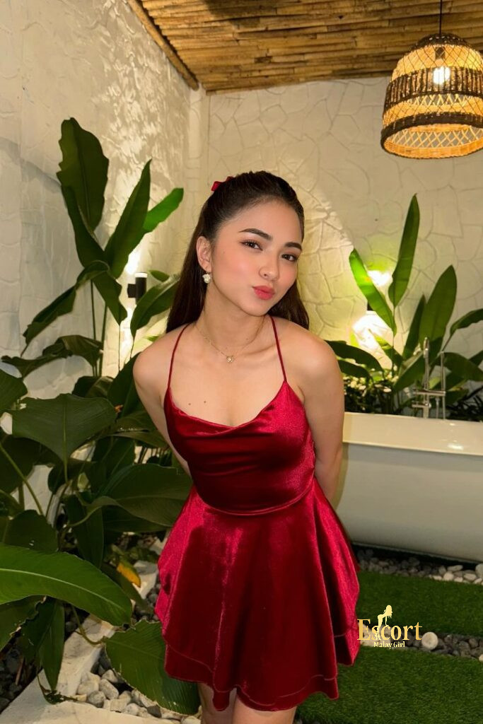 Escort Malay Girl Zanis, a 22yo Malay escort in KL, wears a red velvet dress, standing near a bathtub KL Escort Girl Service