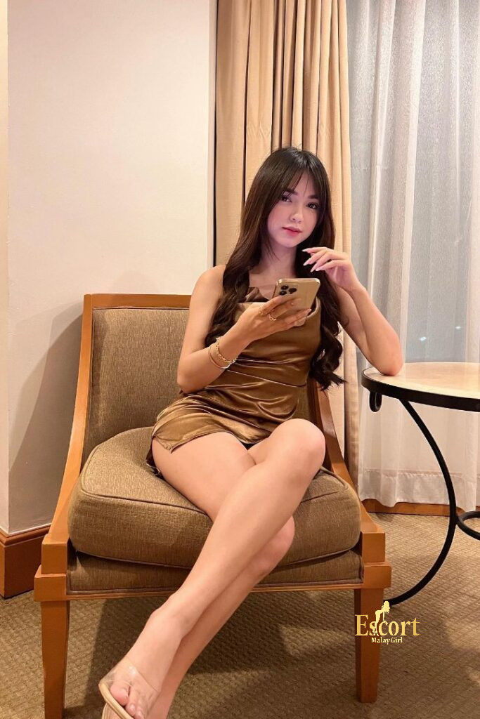 Escort Malay Girl Zanis, 22yo Malay escort in gold dress, texting on phone in elegant room KL Escort Girl Service