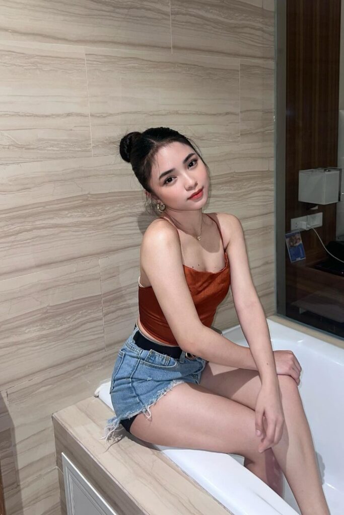 Escort Malay Girl Young woman in denim shorts and a satin top sitting by a bathtub KL Escort Girl Service