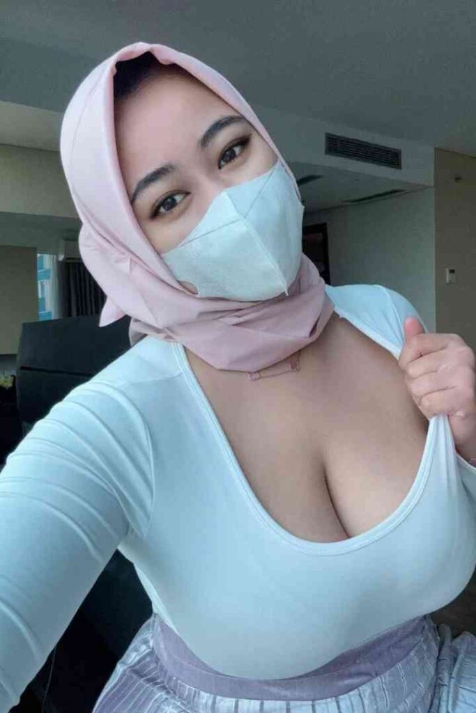 Escort Malay Girl A woman wearing a pink hijab and blue face mask, giving a thumbs up KL Escort Girl Service